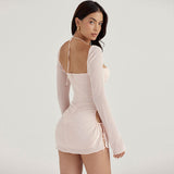 Side view of a woman in a light pink ruched mini dress with sheer long sleeves.