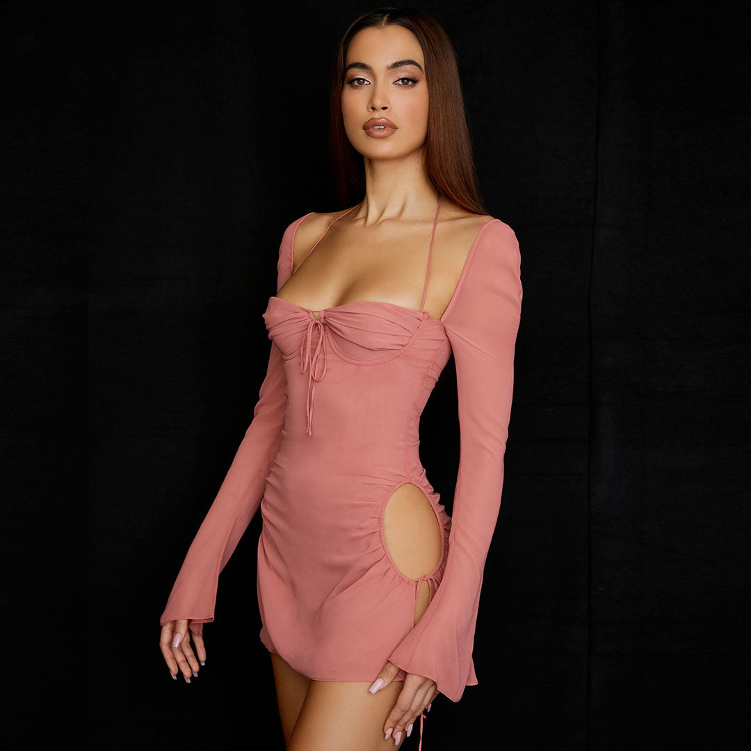 Model wearing a pink ruched mini dress with cut-out sides and long bell sleeves, side view.