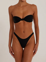 Front view of a woman wearing a black shimmering strapless bikini set with a twisted knot top and high-cut bottoms.