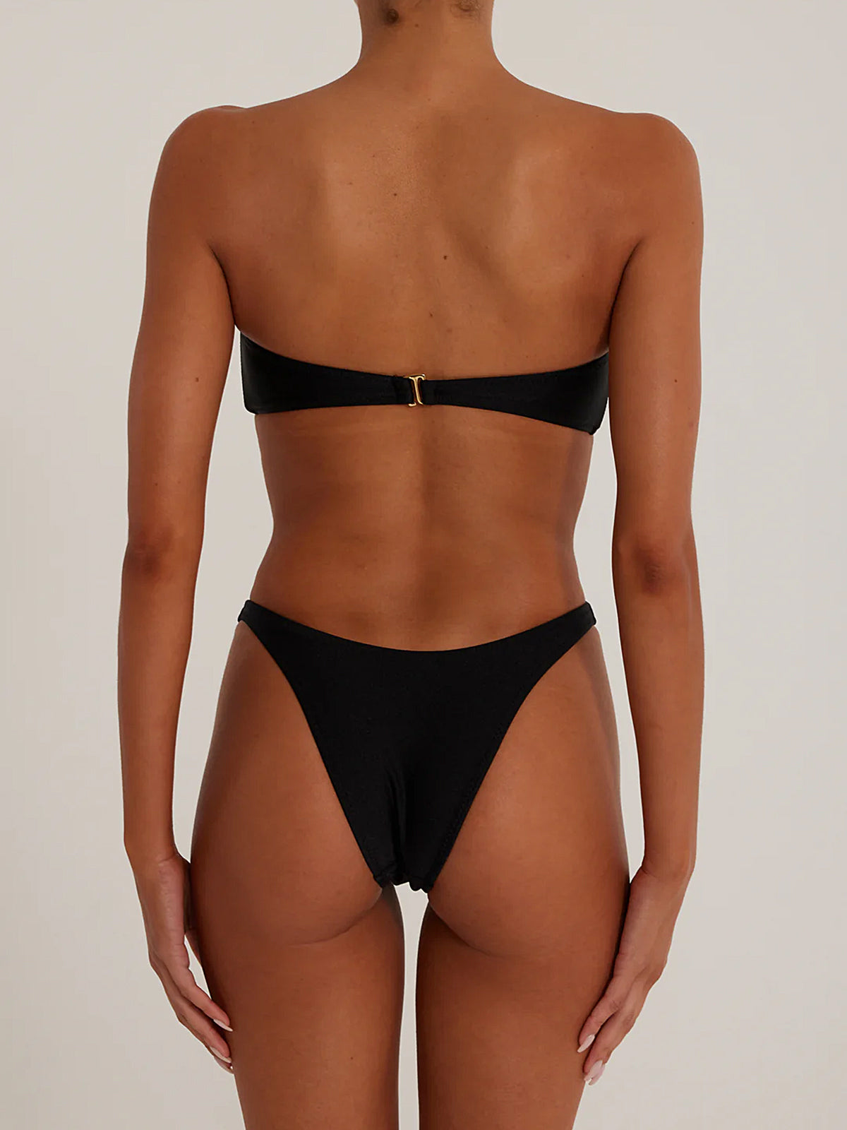 Back view of a woman wearing a black shimmering strapless bikini set with a twisted knot top and high-cut bottoms.