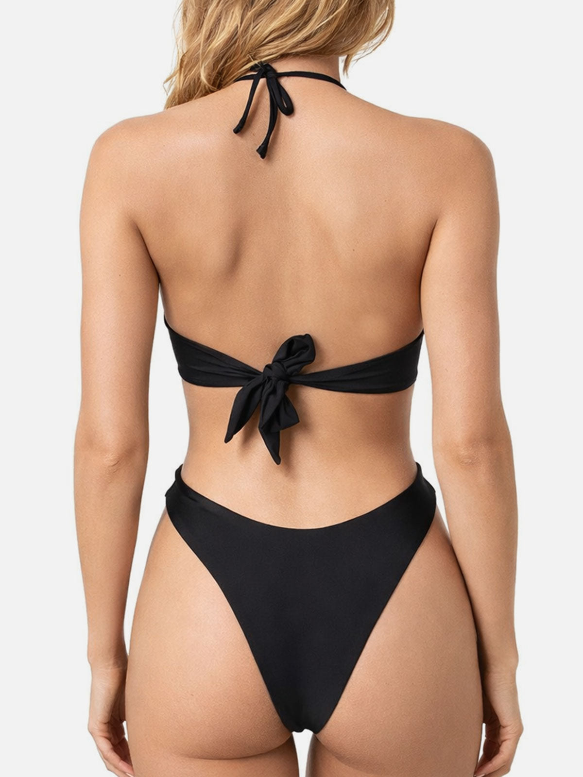 Back view of a woman wearing a black one-piece swimsuit with a halter neck and tie closure.