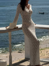 Woman wearing a long-sleeved cream knit dress with a diamond pattern and V-neck, leaning on a railing by the ocean.