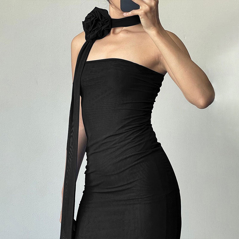 Close-up of a woman wearing a black strapless mesh dress with a prominent black flower accessory on the shoulder.
