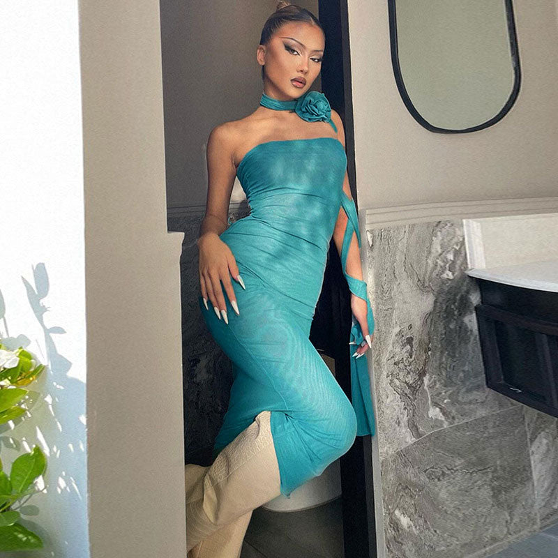Woman wearing a teal strapless mesh column dress with an asymmetrical strap detail and a large floral applique at the neckline.