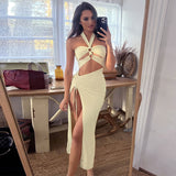 Woman wearing a cream colored two-piece set with halter neckline, cut-out detail, and high slit skirt.