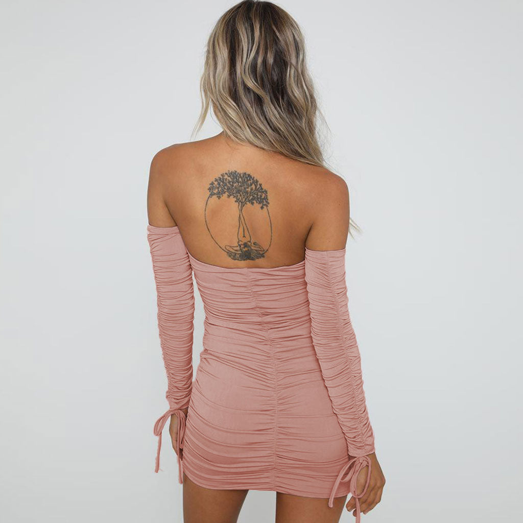 Back view of a woman wearing a pink off-the-shoulder long-sleeved ruched mini dress with a tie front and cutout.