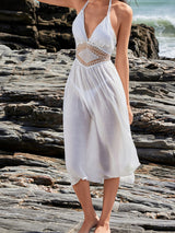Full body shot of a woman in a white sheer midi dress with halter neckline and crochet waist, on a rocky beach.