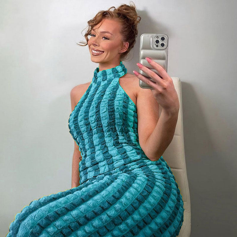 Woman with hair in a bun taking a selfie in a turquoise and blue striped crinkle knit halter maxi dress
