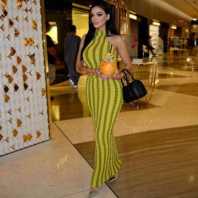 Full body shot of a woman in a green striped bodycon maxi dress with a halter neckline, walking indoors.