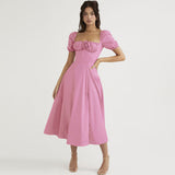 Woman wearing a pink midi dress with puff sleeves and a square neckline, standing against a white background.