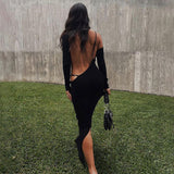 Woman wearing a long-sleeved black midi dress with an open back and cut-out details, standing in a grassy outdoor area.