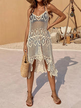 Woman wearing a white crocheted lace beach cover-up over a black bikini, holding a straw bag, standing outdoors.