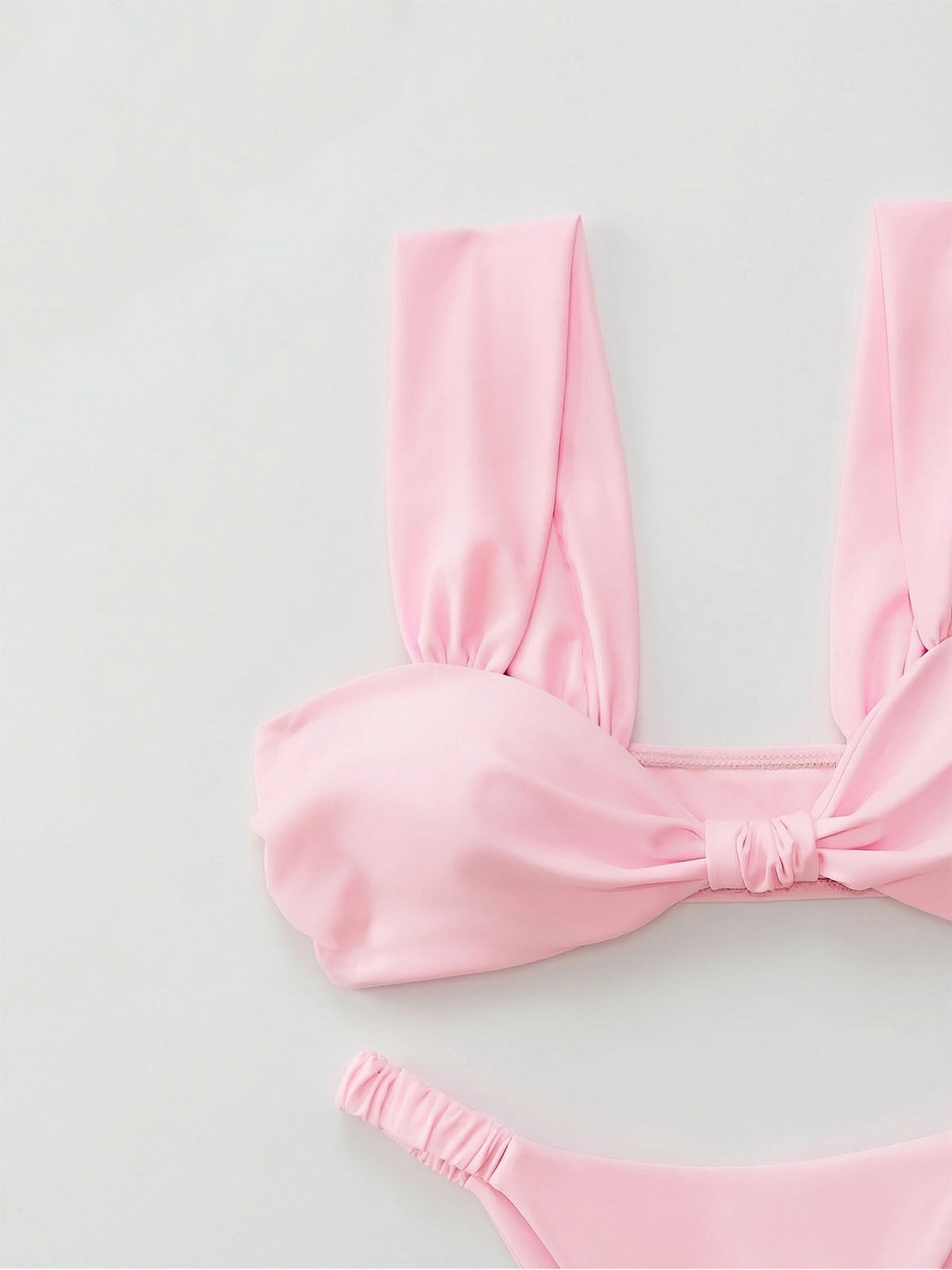 Close-up of a pink bikini top with a twisted front detail and ruched straps, and a matching high-cut bikini bottom.
