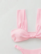 Close-up of a pink bikini top with a twisted front detail and ruched straps, and a matching high-cut bikini bottom.
