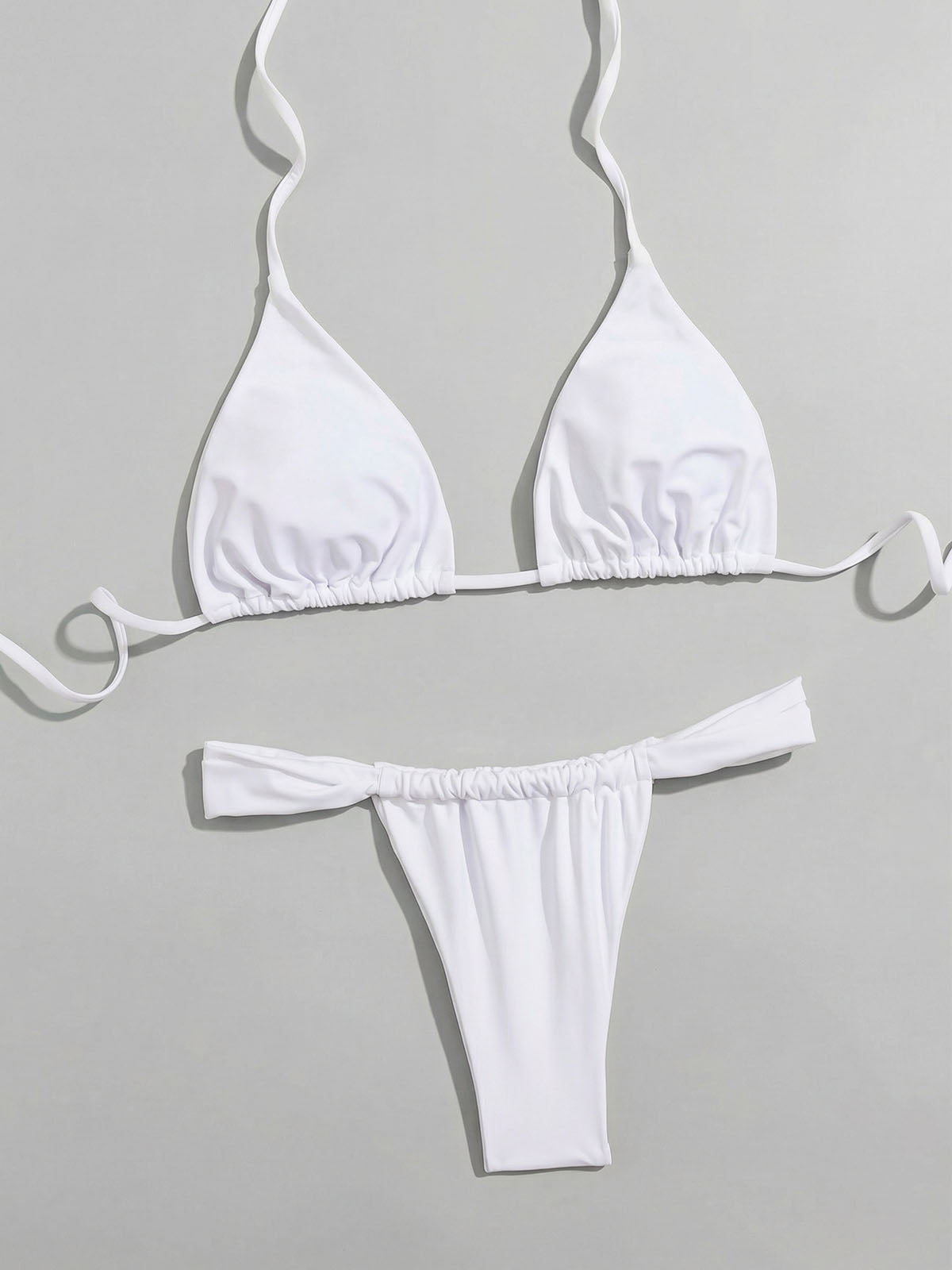 Flat lay of a white triangle bikini top and thong bottom