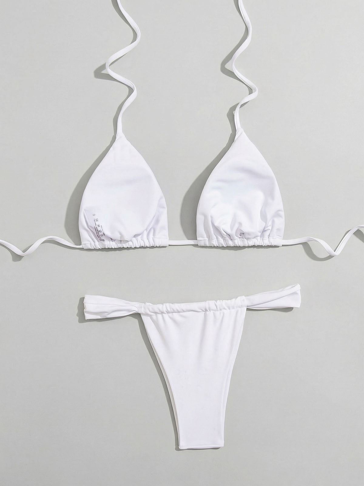 Flat lay of the back of a white triangle bikini top and thong bottom