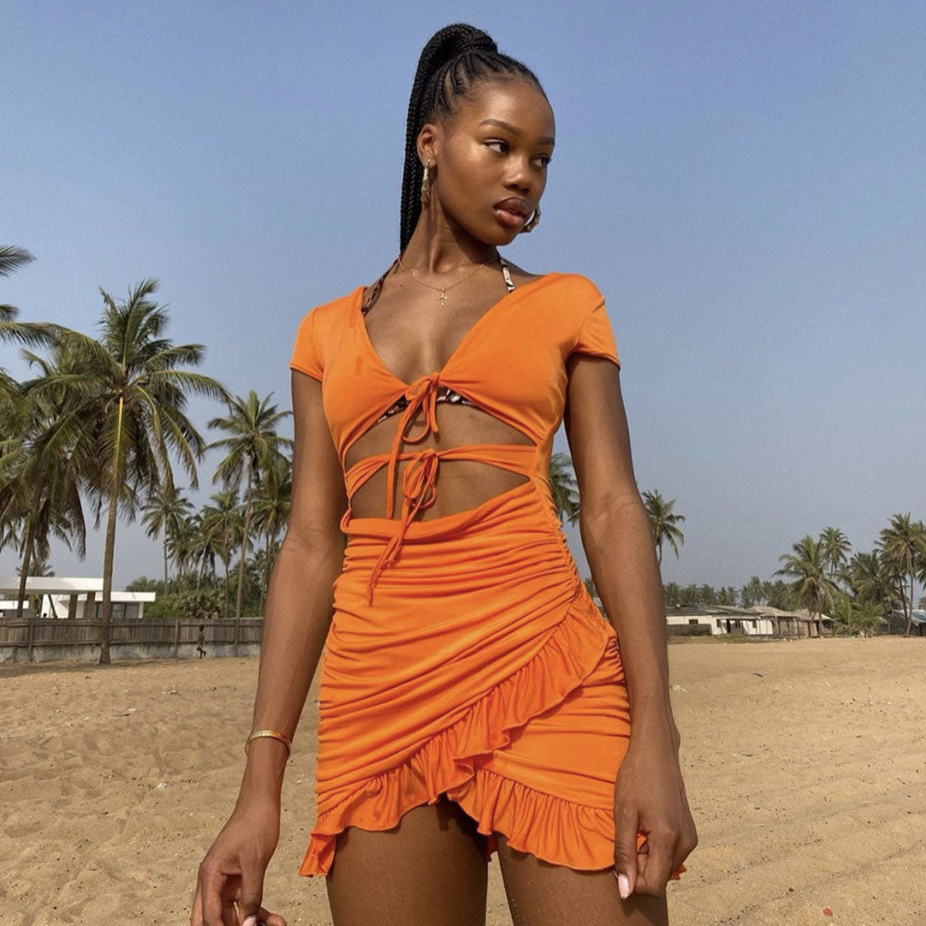 Woman on a beach wearing an orange ruched mini dress with cut-outs