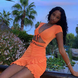Woman posing outdoors in an orange ruched mini dress with cut-outs