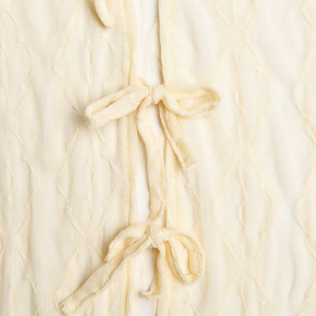 Close-up of the tie closures on the side of a sheer cream midi dress.