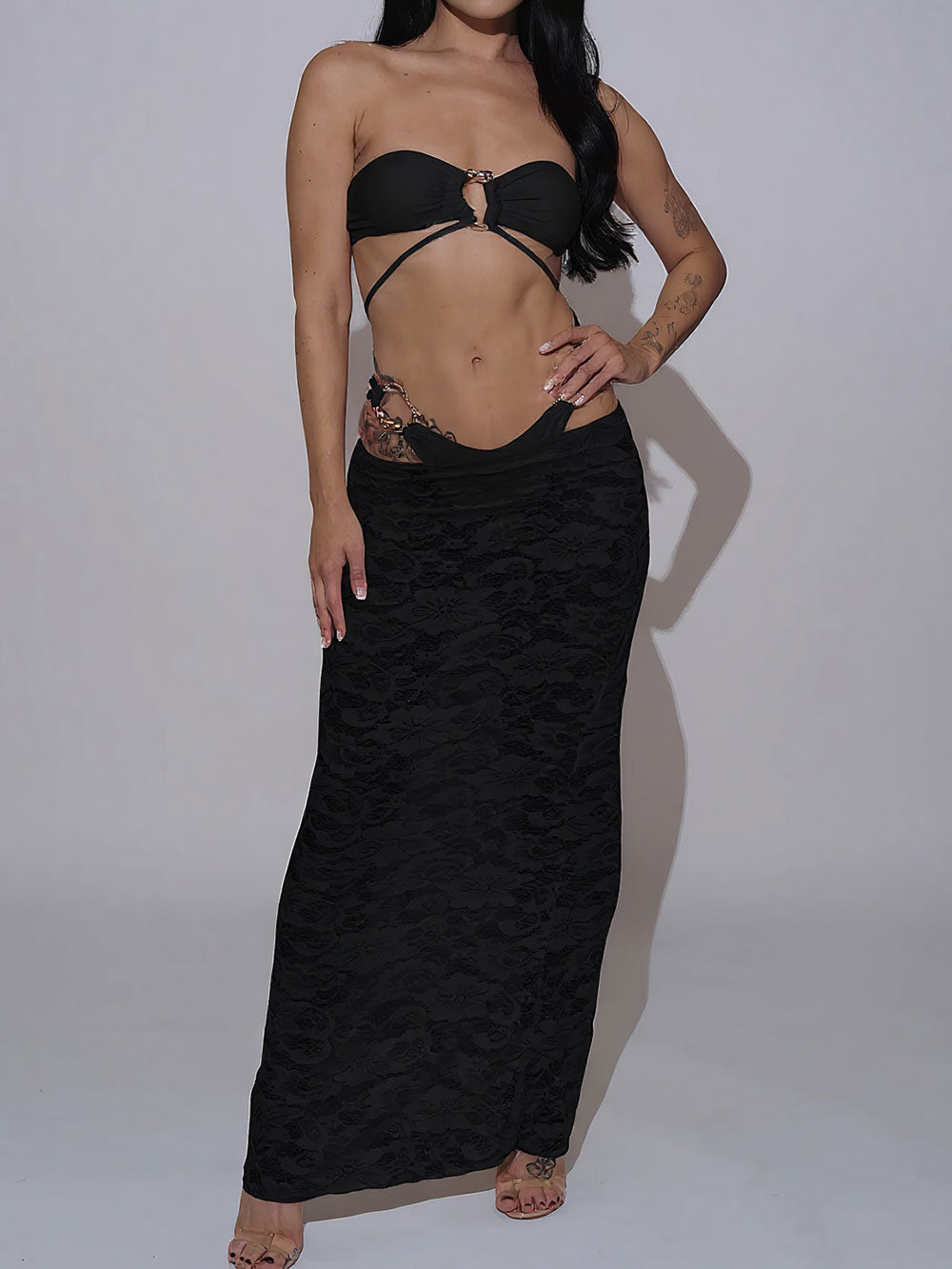 Woman wearing a black strapless bikini top, black high-waisted bikini bottom, and a black sheer lace maxi skirt, front view.