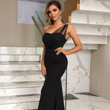 Close-up of a woman in a black one-shoulder gown, highlighting the beaded bodice and sheer illusion neckline detail, on a marble staircase.