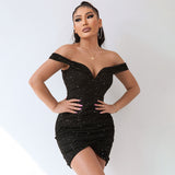 Front view of a woman wearing a black off-the-shoulder sparkly mini dress with ruched detailing and an asymmetrical hemline, with one hand on her chest.
