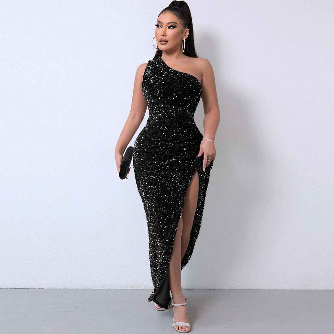 Woman wearing a black one-shoulder sequined maxi dress with a high slit, standing against a white wall.