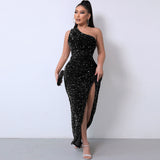 Woman wearing a black one-shoulder sequined maxi dress with a high slit, standing against a white wall.