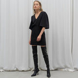Model wearing a black mini dress with flutter sleeves and black knee-high boots, standing against a white backdrop.