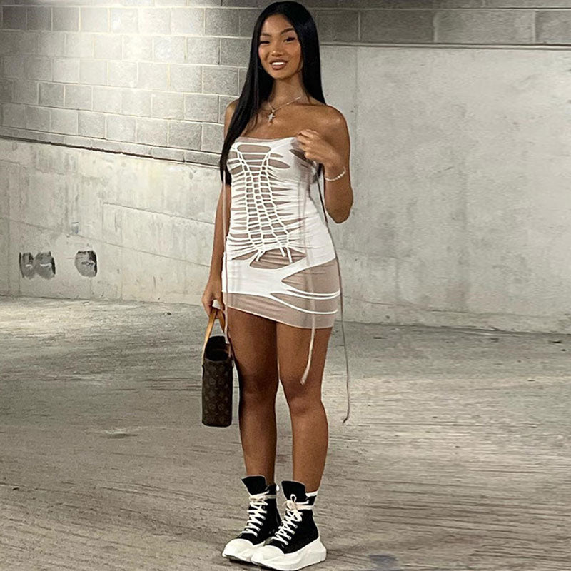 Woman wearing a white strapless bodycon mini dress with cut-out details and a lace-up front, paired with black and white high-top sneakers and carrying a brown designer handbag.