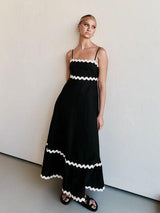 Woman posing in a black maxi dress with white scalloped trim and spaghetti straps.