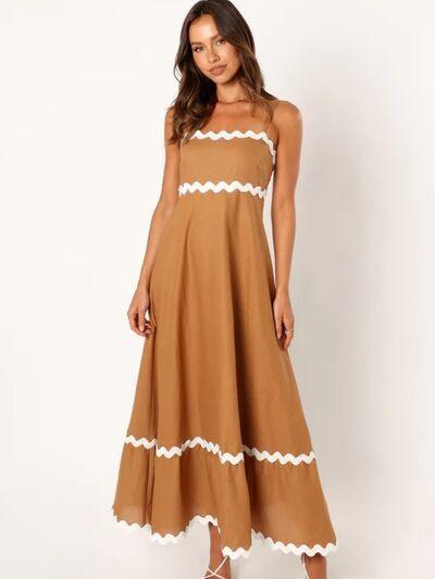 Woman wearing a tan maxi dress with white scalloped trim and spaghetti straps.