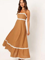 Woman in a tan maxi dress with white scalloped trim, with a white background.