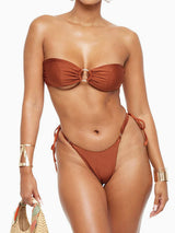 Woman wearing a strapless brown bikini with gold ring detail and adjustable side ties