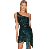 Woman wearing a short, emerald green sequined one-shoulder dress with a belted waist and asymmetrical hem.