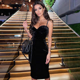 Woman in a black velvet midi dress with spaghetti straps standing on a modern staircase.