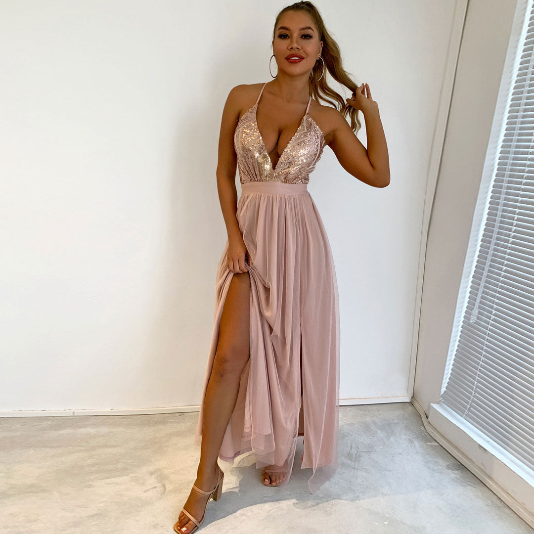 Woman in a blush pink formal dress with a sequined bodice and a high slit, posing with her hand on her hip.