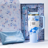 An open floral-patterned gift box containing a light blue Stanley Quencher H2.0 Tumbler, a straw, and a soft blue cloth pouch.