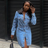 Woman in a denim shirt dress with a belted waist, standing against a black slatted background.