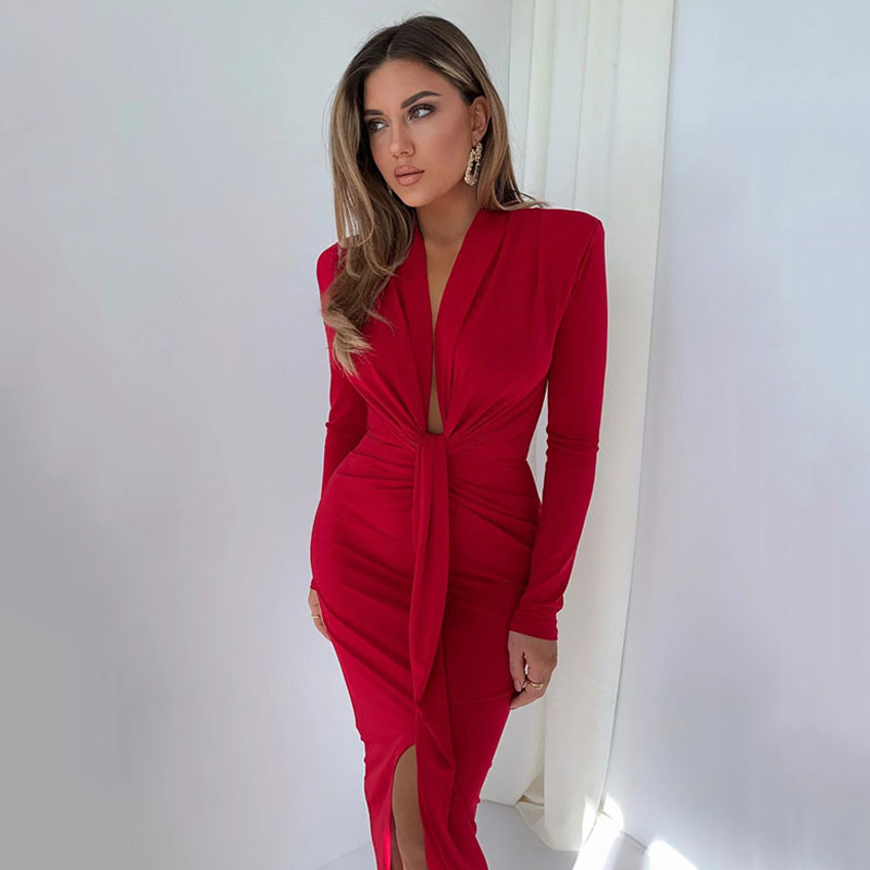 Full body shot of a woman wearing a long-sleeved red ruched sheath dress with a plunging neckline and thigh-high slit.