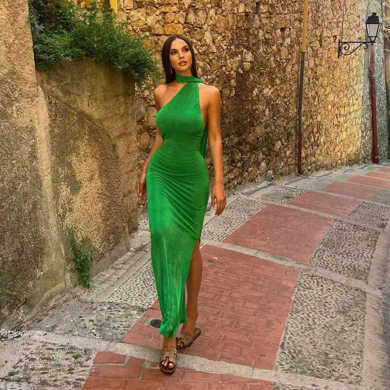Woman wearing a green one-shoulder velvet maxi dress with a high slit walking down a cobblestone street.