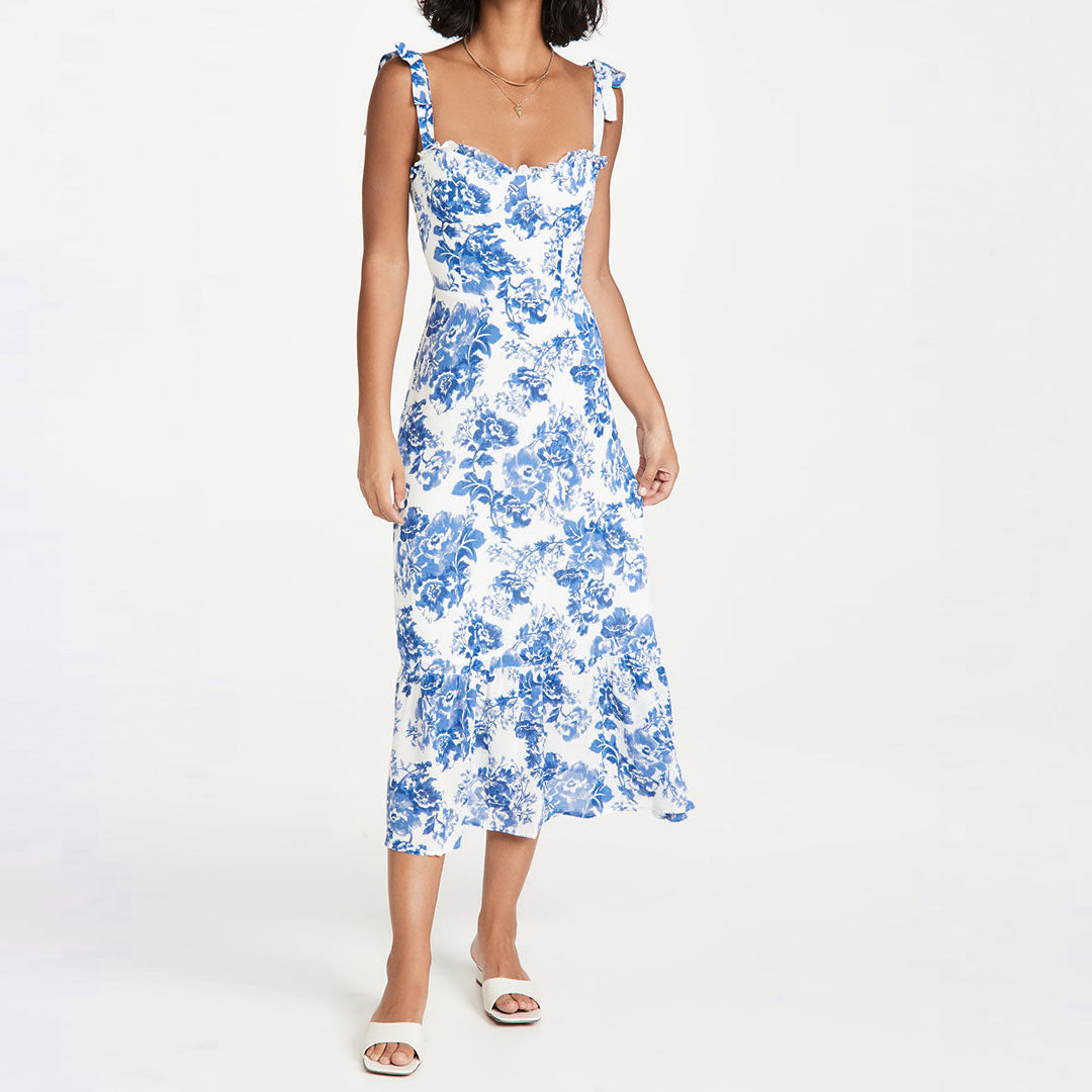 Woman wearing a white midi dress with a blue floral print and tie shoulder straps, standing front view.