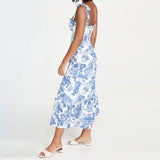 Woman wearing a white midi dress with a blue floral print and tie shoulder straps, standing side view.
