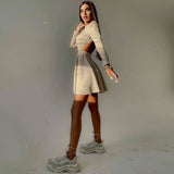 Woman wearing a long-sleeved beige ribbed knit fit and flare dress with a crew neck and cut-out detail, posing with one leg extended.