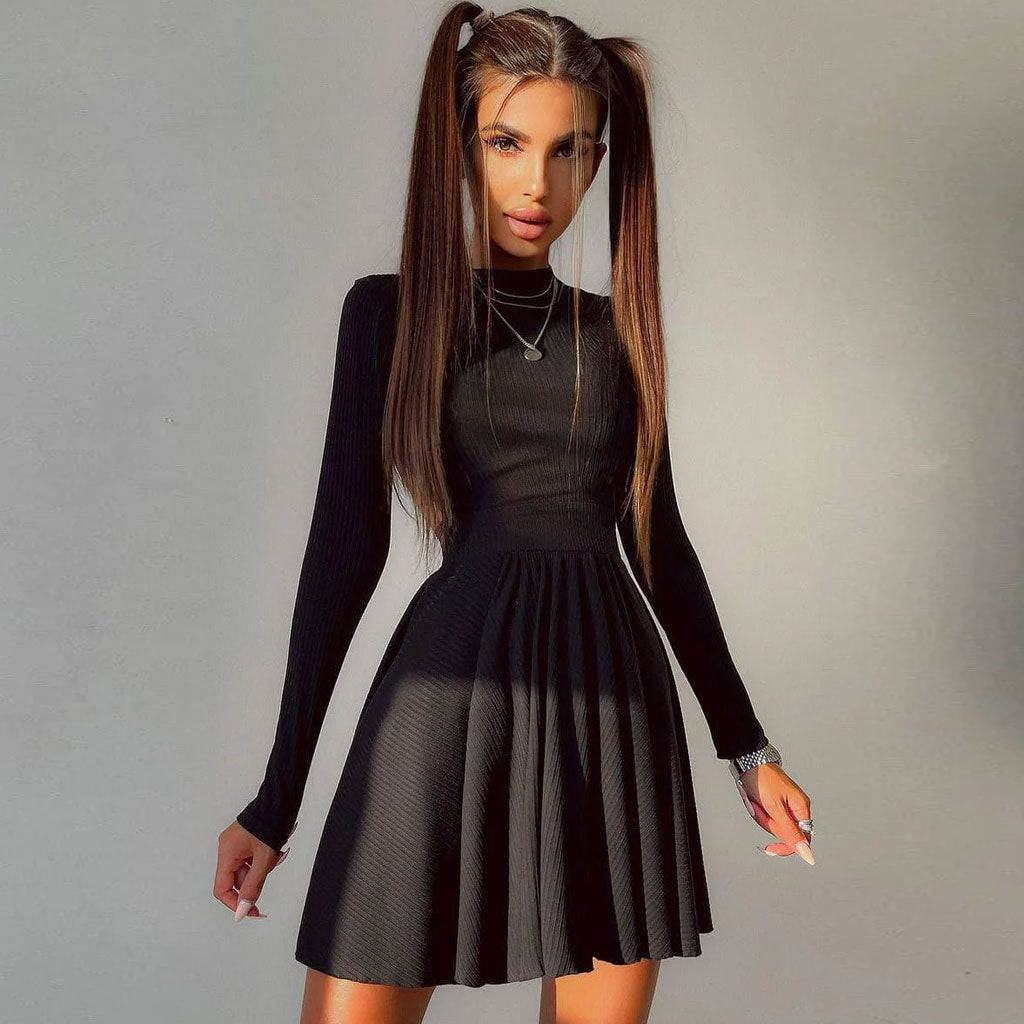 Woman wearing a black long-sleeved ribbed knit dress with a mock neck and a fit and flare skirt, standing in front of a light gray background.