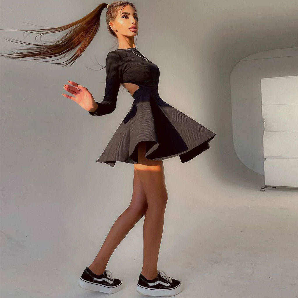 Woman wearing a black long-sleeved ribbed knit dress with cut-out details and a fit and flare skirt, walking in a studio with a white background.