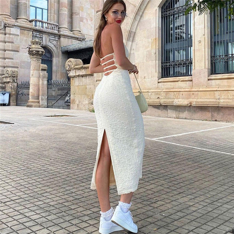 Rear view of a woman in a white textured midi dress with an open back featuring multiple straps, and a side slit.