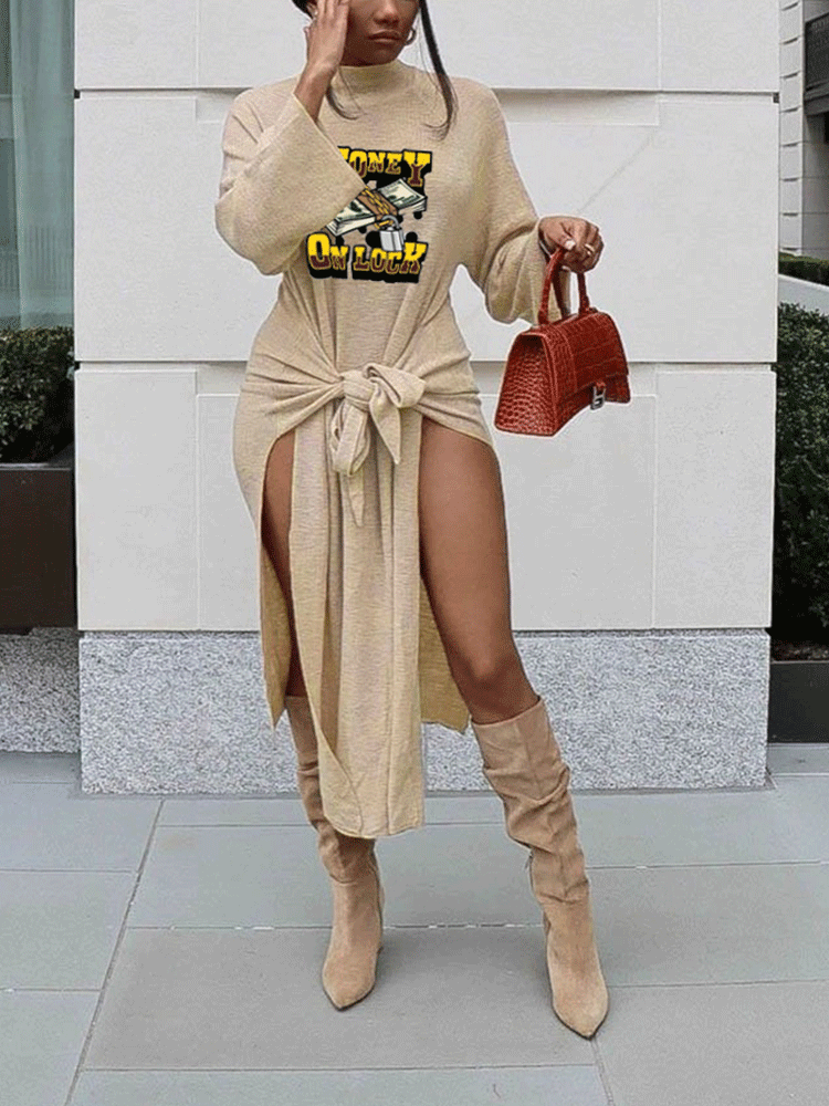 Woman wearing a tan long-sleeve mock neck dress with a tie waist and high slits, featuring a graphic print of money. She is also wearing tan knee-high boots and carrying a red textured handbag.