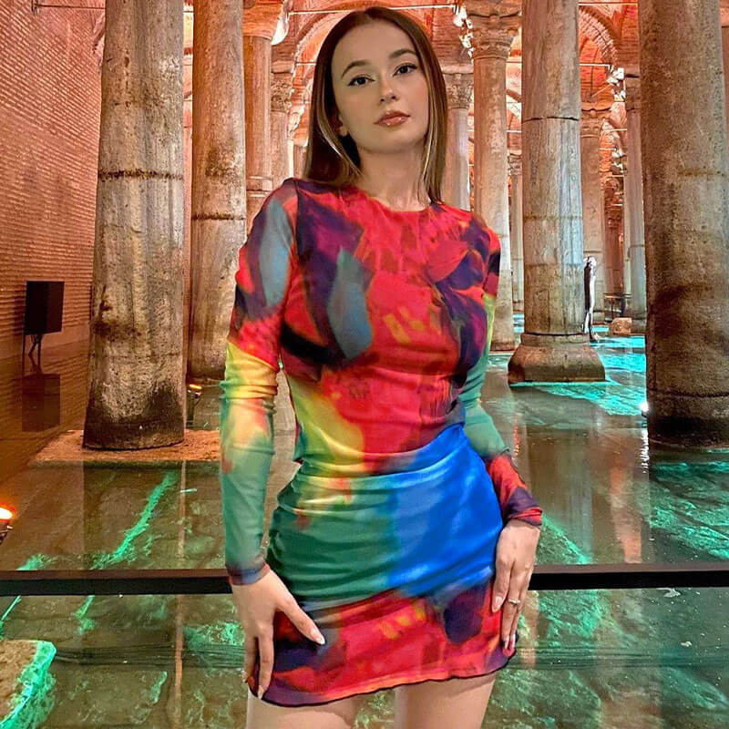 Woman wearing a colorful tie-dye mesh mini dress with long sleeves and a crew neck.