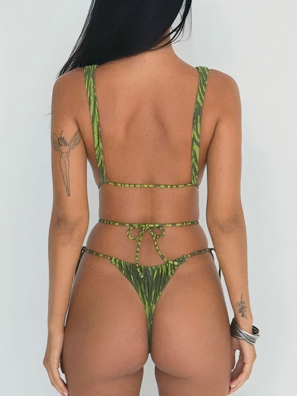 Back view of a woman wearing a green patterned one-piece swimsuit with a low back and string bikini bottom